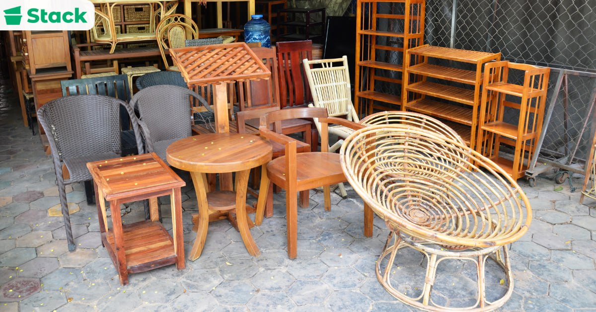Assorted wooden furniture including side tables, dining chairs, shelving units and a rattan chair lined up outdoors before a move