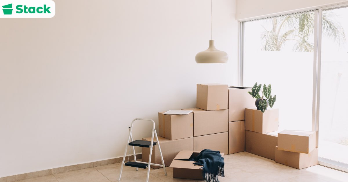 Cardboard moving boxes stacked in a bright, nearly empty living room beside a step ladder, packed and ready for moving day