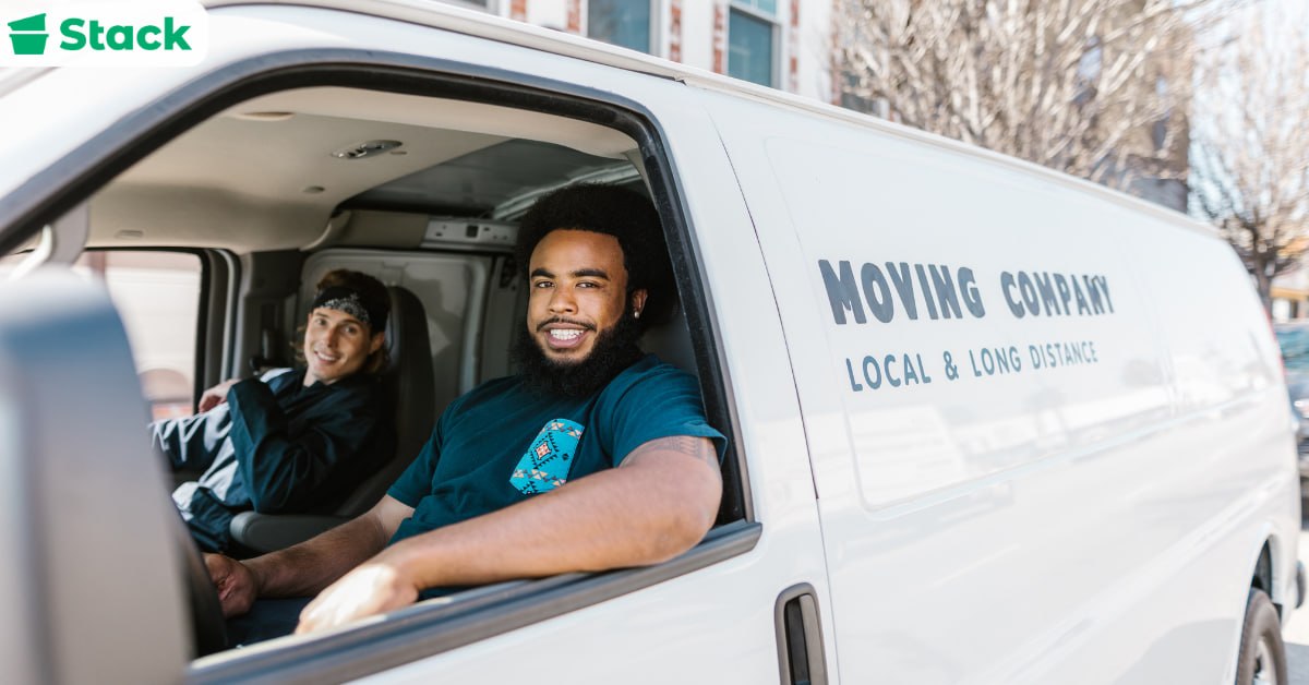 Two smiling movers sitting in the cab of a white moving van marked Moving Company, Local and Long Distance