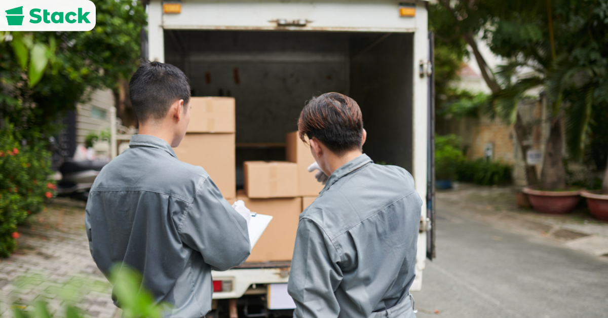 Movers loading boxes while homeowner checks list for moving out